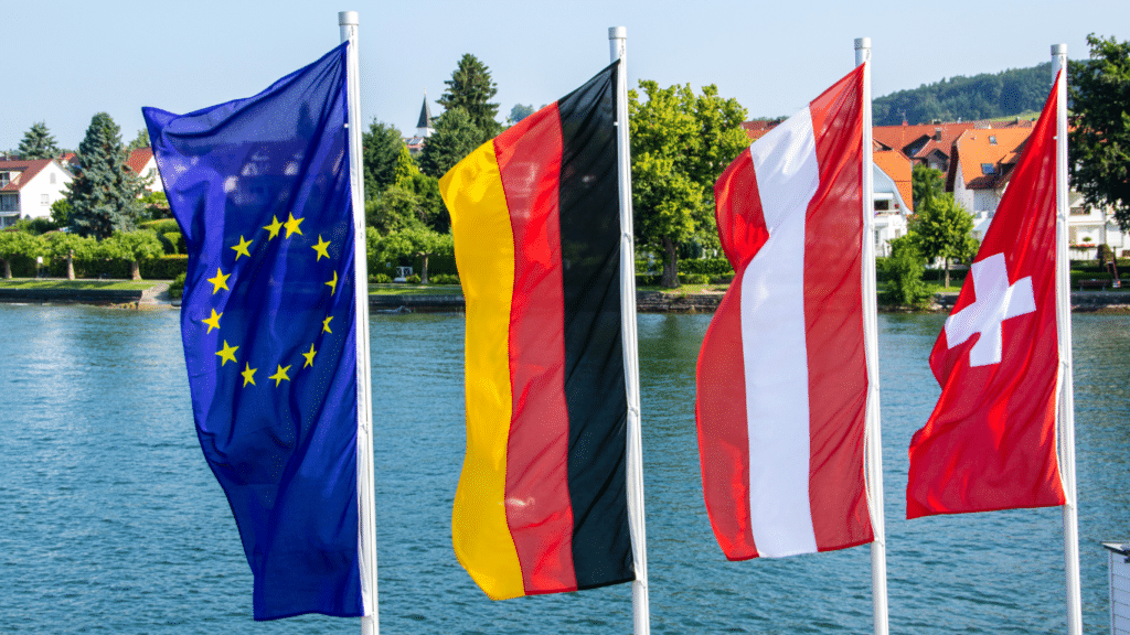 Die Flaggen der EU, Deutschlands, Österreichs und der Schweiz mit dem Bodensee im Hintergrund